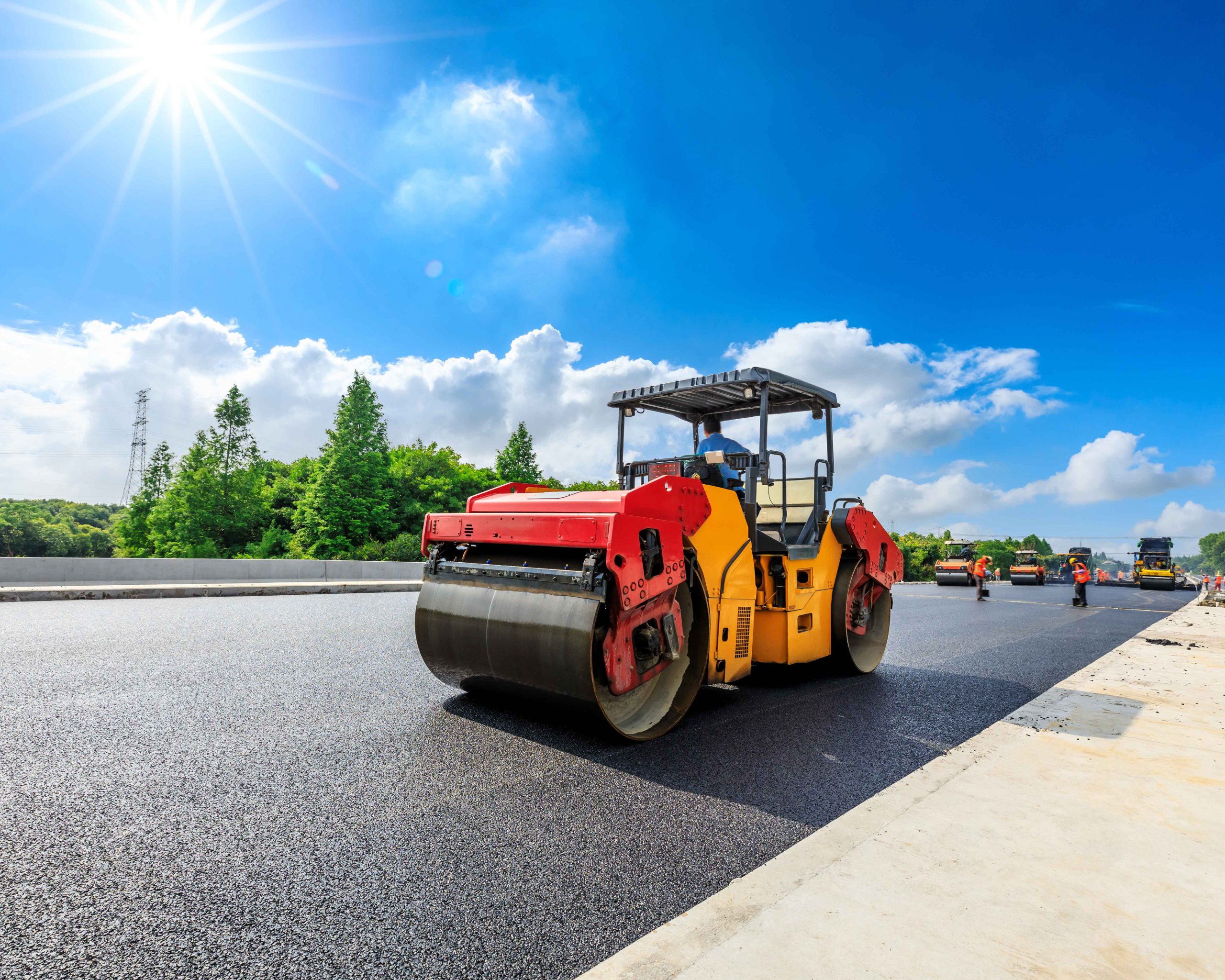 A construction crew operates rollers to complete an asphalt paving job.