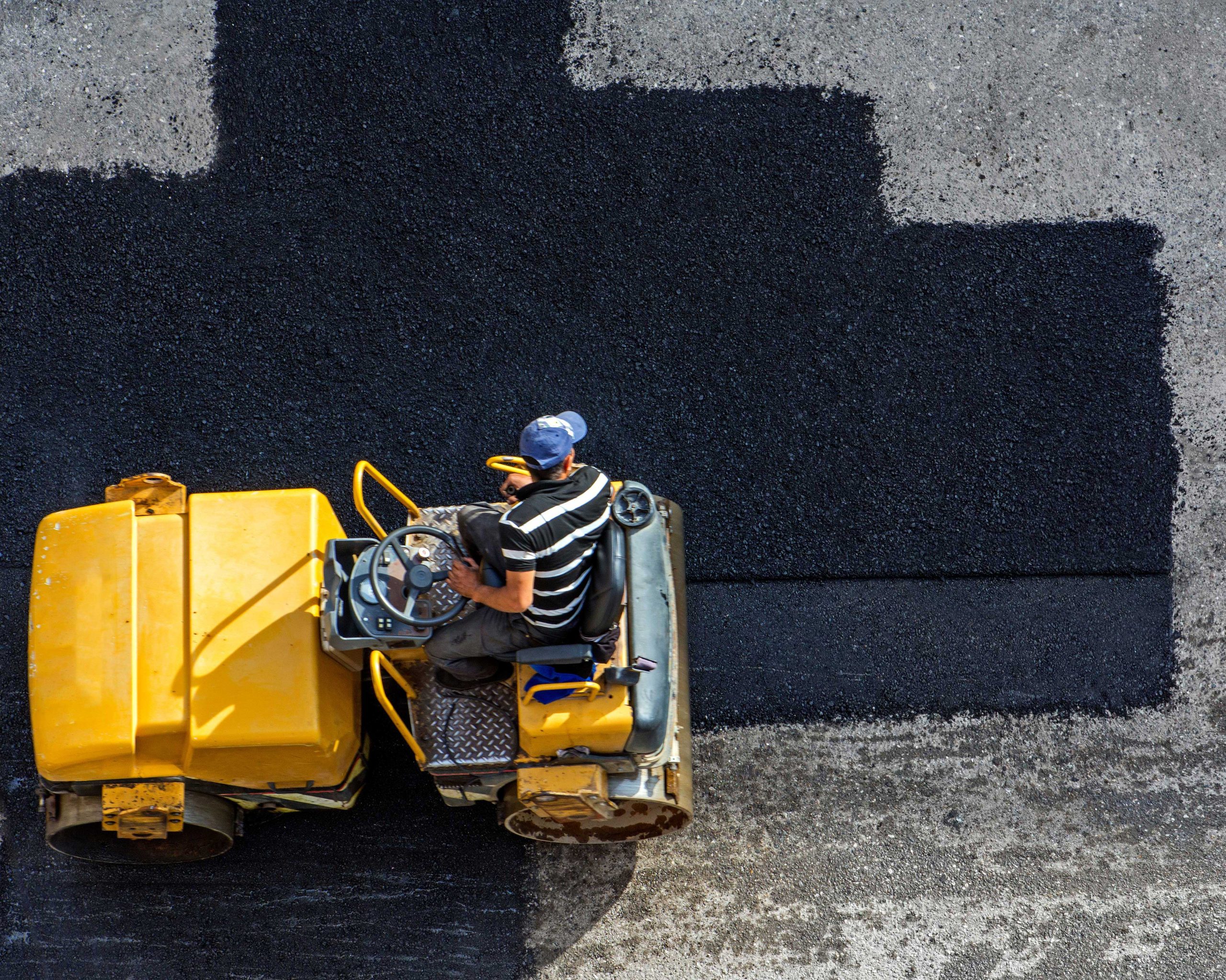 A commercial asphalt contractor operates a roller to repave an asphalt parking lot.